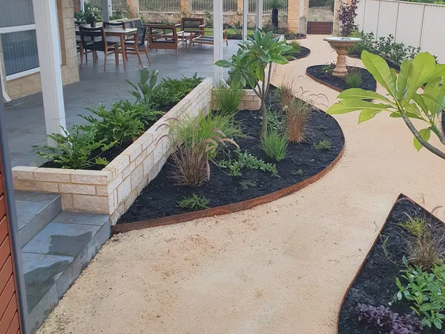 Curved garden beds with limestone retaining, corten steel edging and native plants beside a crushed limestone path in Viveash